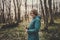 Toned photo of happy hiking middle-aged woman in blue jacket standing and resting in evening spring forest