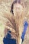 Toned photo of woman hide behind large fluffy bouquet made of dried yellow bushgrass holding in hand.