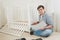 Toned photo of young man assembling furniture by himself in new