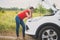 Toned photo of young woman standing at broken car on countryside road and looking at overheated engine