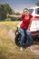 Toned photo of young woman wirh broken car witting on spare wheel and hitch0hiking