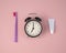 Toothbrush, tube of toothpaste and alarm clock on a pink background. Time to brush your teeth.