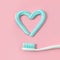 Toothbrushes and turquoise color toothpaste in shape of heart on pink background.