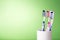 Toothbrushes in white cup on light green background