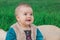 toothless baby in a multi-colored dress sitting on a bedspread on lawn