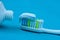 Toothpaste on a toothbrush against a white tube on a blue table