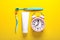 Toothpaste, toothbrushes and alarm clock on yellow background, flat lay