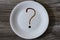 Top above overhead close up view photo of white plate crockery on wooden table. A plate with question mark on it, written with cho