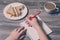 Top above overhead close up of writing hand in a notebook and tasty cheese sandwich on a round plate, cup of latte. Wooden backgro