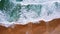 Top aerial view of foam waves break on orange colored sand beach. Bird`s eye view of emerald green blue ocean water