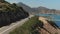 Top Aerial View Of A Red Car Drive On The Road Near Sea. Aerial Drone shot of cars driving on beach and coast rooad.