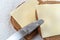 Top close view of a butter knife atop two slices of wheat bread with margarine and cheese on paper towels