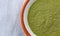 Top close view of organic powdered wheat grass in a small bowl on a gray marble counter top