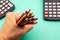 Top closeup of a hand holding colored pencils with black calculators around on the green background