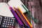 Top closeup of a notebook with a pack of colored pencils and a black calculator, wooden background