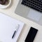 Top of desk with notebook pen smartphone plate with doughnut and laptop keyboard