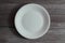 Top direct above overhead close up view photo of an empty white ceramic round plate on grey wooden background. Hunger dieting skin