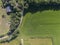 Top down aerial view of cultivated green field with tractor tracks and curved road