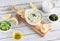 Top down view of a bowl of tzatziki dip surrounded by ingredients used to make the dip and pita bites for dipping.