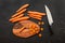 Top down view, chopping board, chef knife and carrot, some of them sliced, on dark marble board