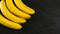 Top down view, four bananas on black slate board, space for text on right side