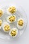 Top down view of a glass plate of creamy deviled eggs, ready for eating.