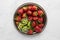 A top down view of a metal tray of strawberries and a small bowl of sliced kiwis. A complimentary colour concept.