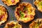 Top-down view of a mini quiche with a flaky crust, runny egg filling, and crisp bacon bits, served in a cute muffin tin