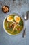 Top down view of a single bowl of Soto Ayam translation: Indonesian chicken soup with a spoon on a textured blue background