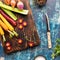 Top down view of a wooden cutting board topped with raw vegetables used in cooking mirepoix. Instagram crop.