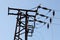 Top of electrical transformer pylon, photo of electric wires against blue sky.