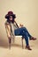 Top off your outfit with the perfect hat. Studio shot of a young woman sitting on a chair and wearing a pile of hats