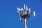 Top part of cell phone communication tower with multiple antennas against a blue sky