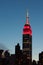 Top part of the Empire state building at sunset. Lights are colo