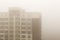 Top part of highrise modern apartment building facade during heavy fog weather