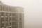 Top part of highrise modern apartment building facade during heavy fog weather