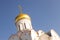 Top part of white Orthodox church with sunlit gilded dome against clear blue sky