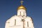 Top part of white Orthodox church with sunlit gilded dome against dark blue sky