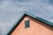 The top of the pink dwelling with a corner roof. A small structure against an overcast sky