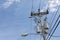 Top of a power pole with multiple transformers, insulators, wires, and a street light against a blue sky with clouds, creative cop