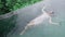 Top shot view of a mixed-race girl in a soft pink evening dress who is swimming on her back in a pool with emerald green