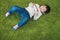 Top view of asian cute and smart little boy lying on geen floor while using or playing game from cell phone device with attention