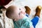 Top view baby in jeans and shoes sits near a Christmas tree, toys balls lie around