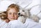 Top view of beautiful blonde little girl lying with white schnauzer puppy dog on white bed. Friendship concept.