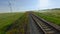 Top view of beautiful railway on background of green field. Shot. Wind farm near beautiful railway in green field