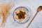 Top view of a beef dish with dumplings on a white tablecloth with a wooden spoon and wheat sheaves