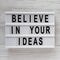 Top view, `Believe in your ideas` words on lightbox over white wooden background. Flat lay, from above, overhead. Copy space