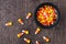 Top view of a black ceramic cauldron of holiday candy corn on a rustic wood background, a few corns spilled on background