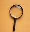 Top view Black round magnifying glass on orange background. used for searching or expanding books.