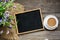 Top view of a black slate board in a wooden frame, a white cup with a saucer and coffee with milk, a bouquet of wild flowers on an